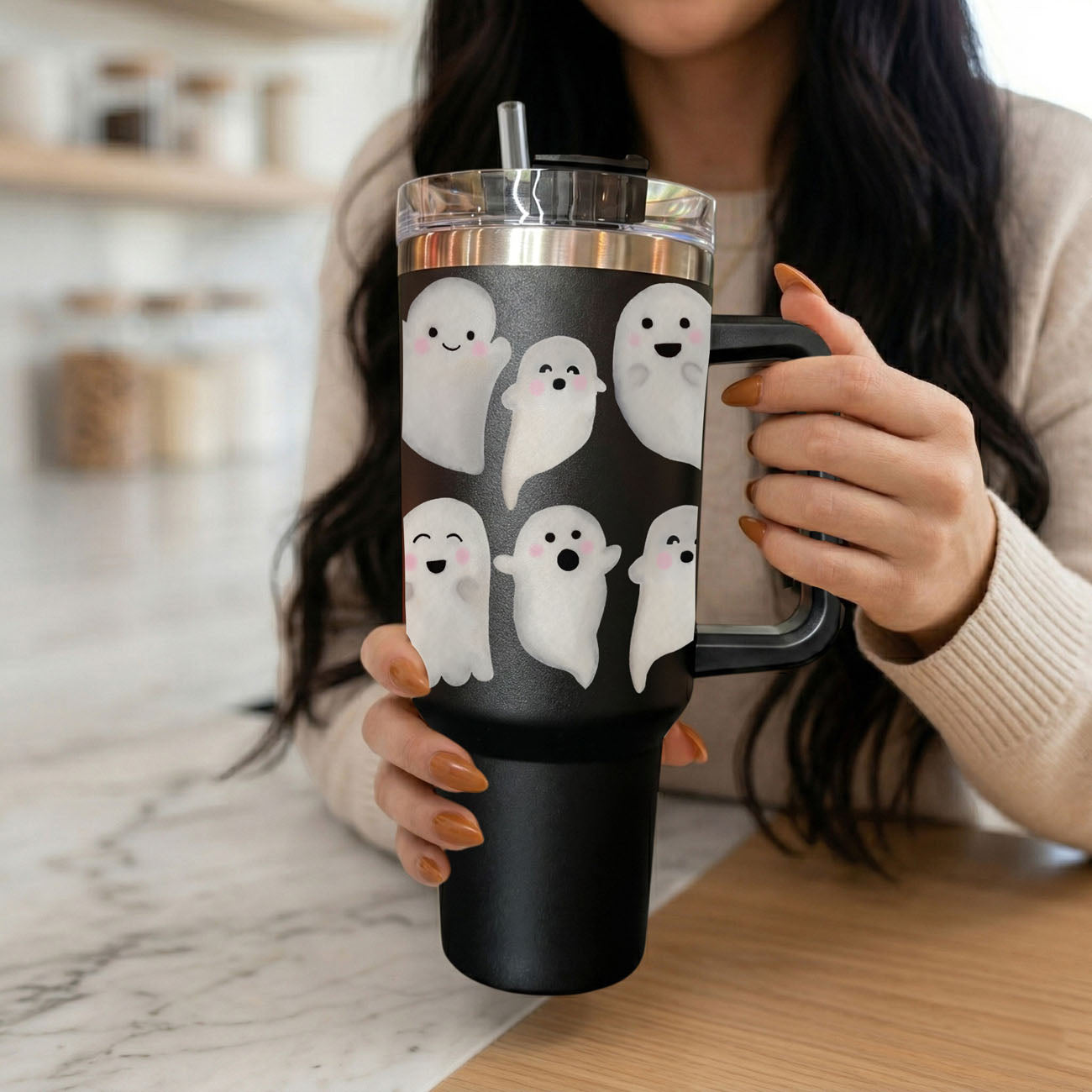 Person holding a black tumbler with ghost designs in a kitchen setting
