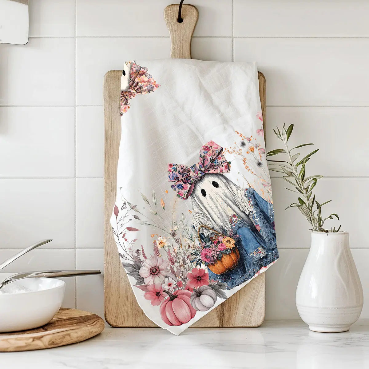 Decorative kitchen towel with a ghost and floral design on a wooden cutting board.