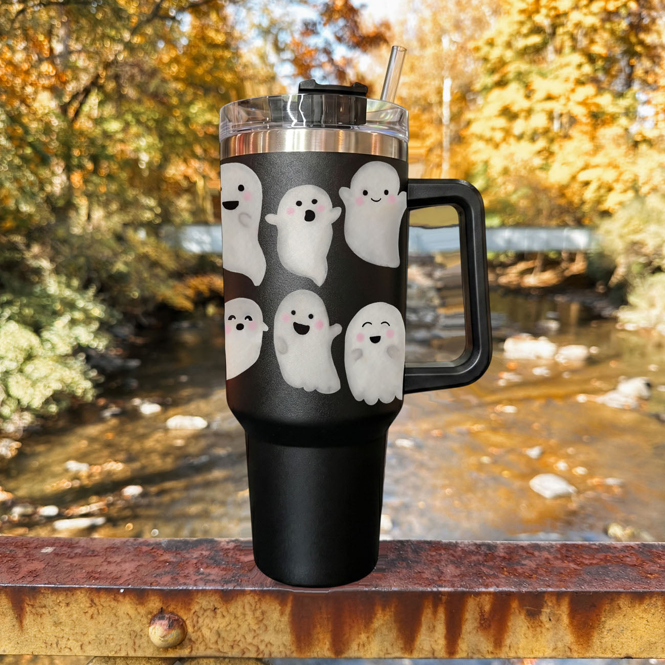 Black tumbler with ghost designs outdoors by a stream