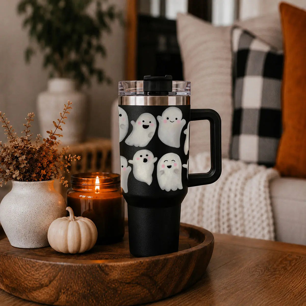 Black travel mug with ghost design on a wooden surface with decorative items.