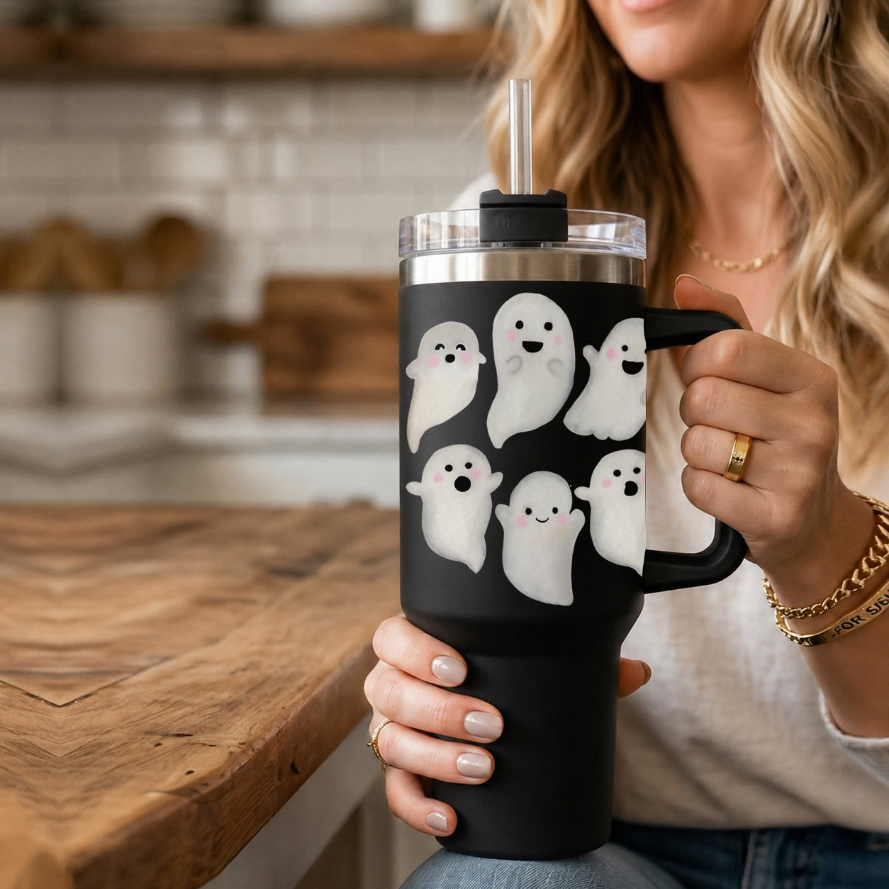 Person holding a black tumbler with ghost designs in a kitchen setting