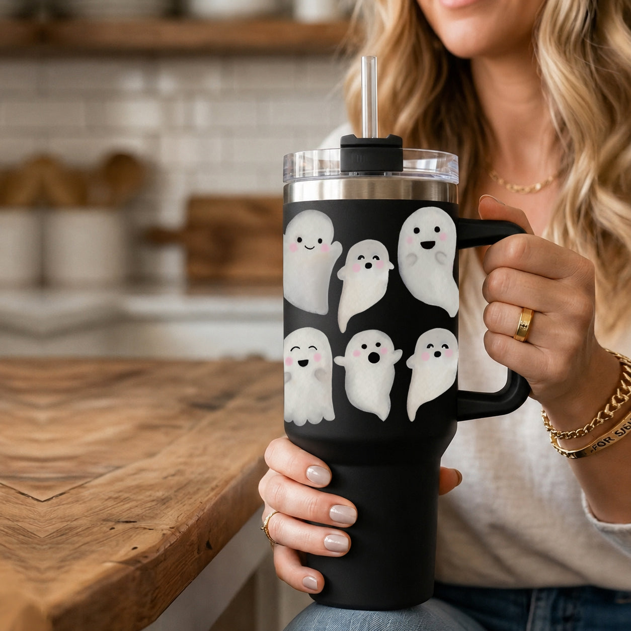 Person holding a black tumbler with ghost designs in a kitchen setting