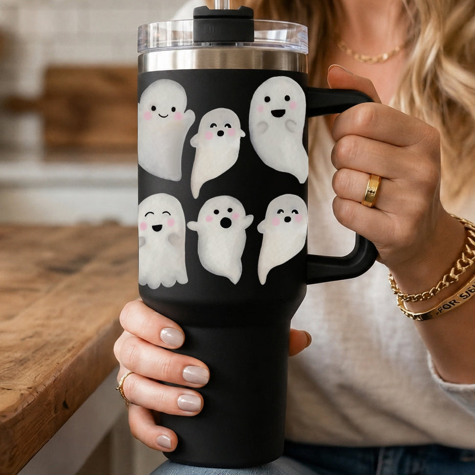 Person holding a black tumbler with ghost designs in a kitchen setting