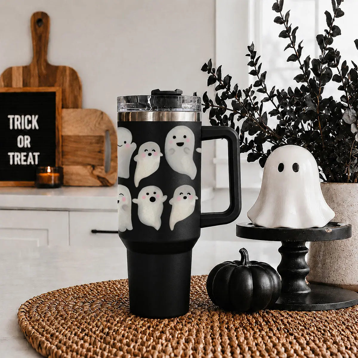 Black tumbler with ghost designs on a woven mat, surrounded by Halloween decor.