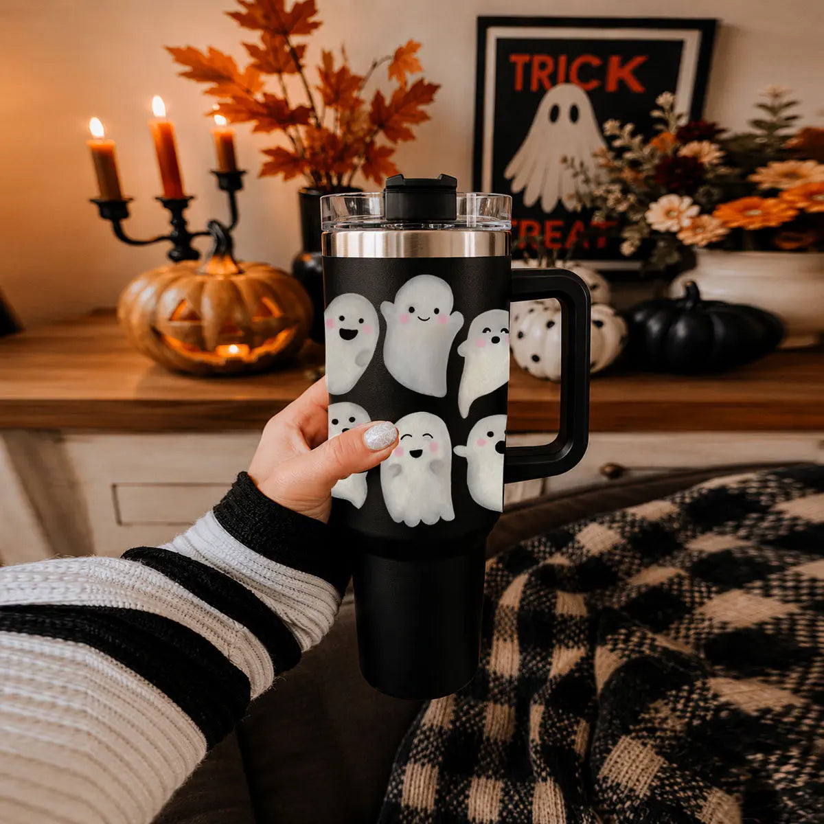 Person holding a black tumbler with ghost designs in a cozy room decorated for Halloween.