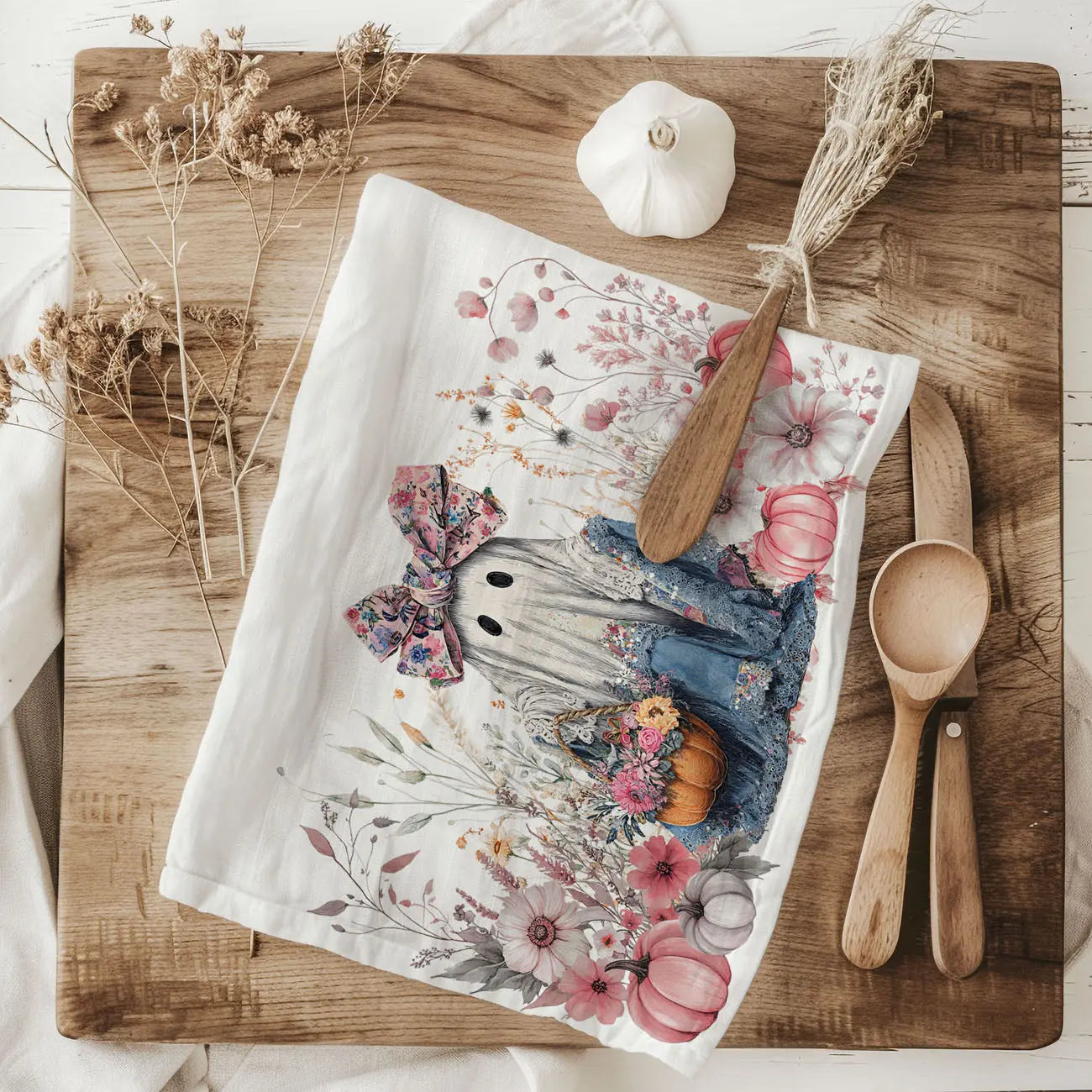 Decorative kitchen  towel with a ghost design, surrounded by wooden utensils and a bulb of garlic