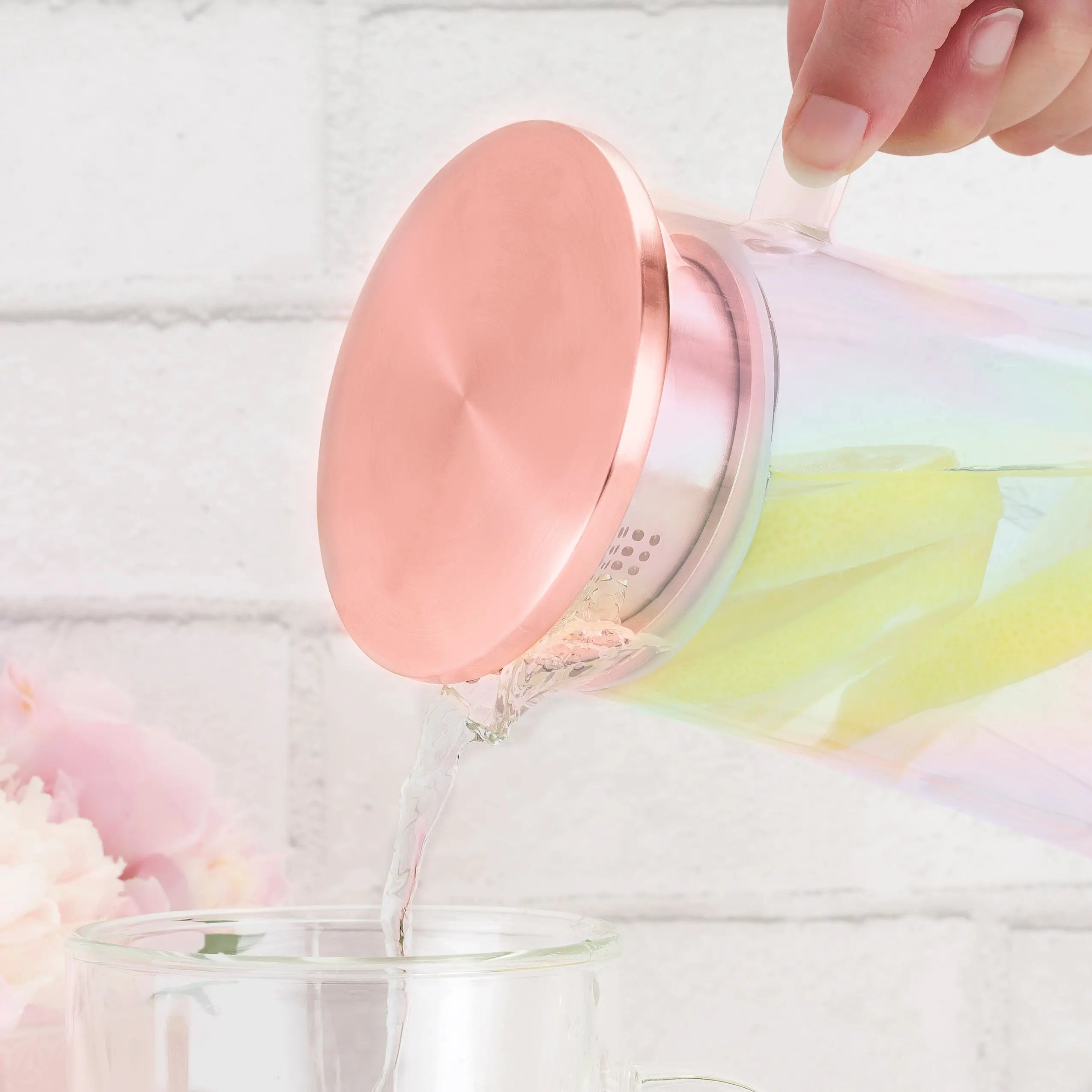 Pink glass pitcher being filled with a colorful liquid on a soft white background