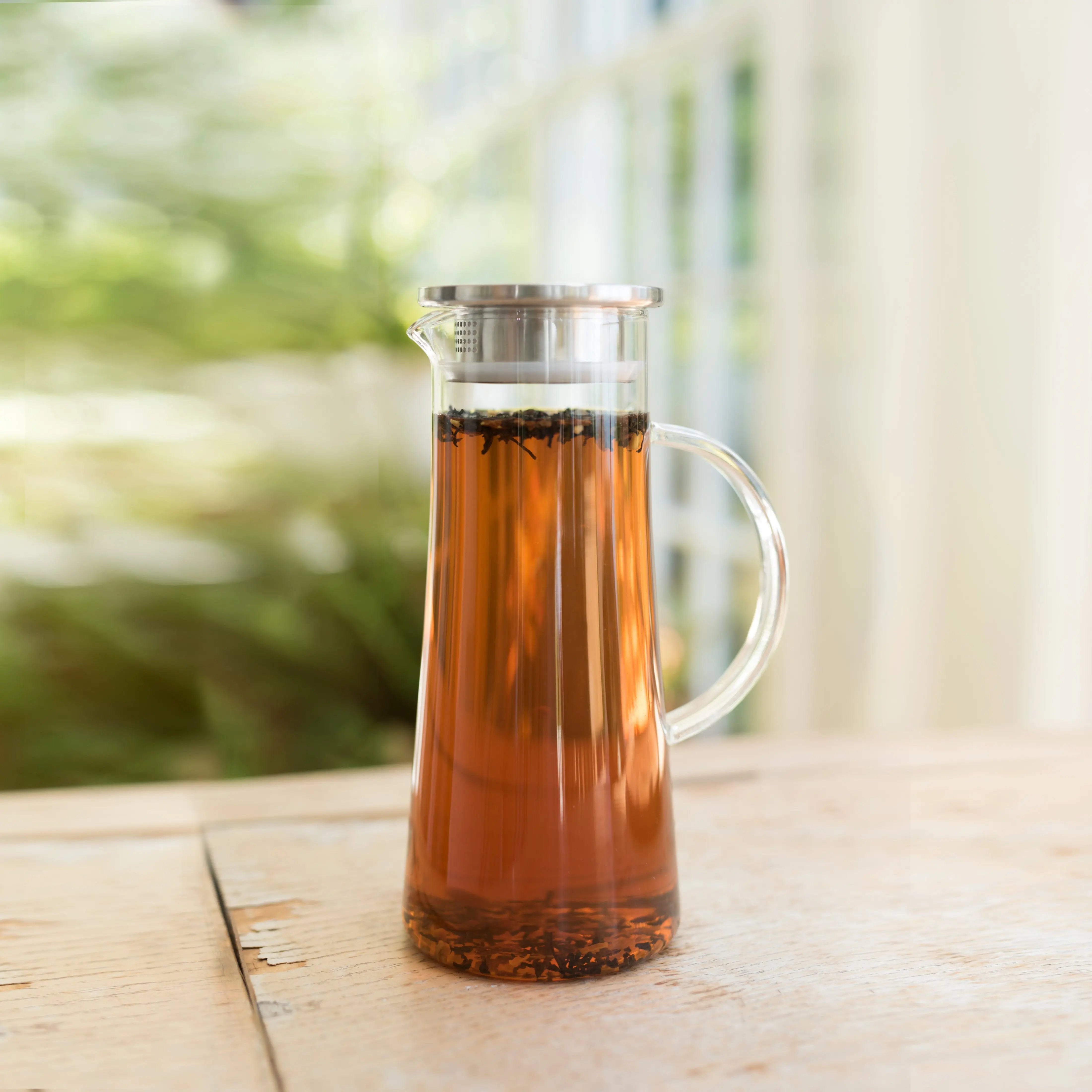 Glass pitcher filled with iced tea on a wooden surface with a blurred green outdoor background
