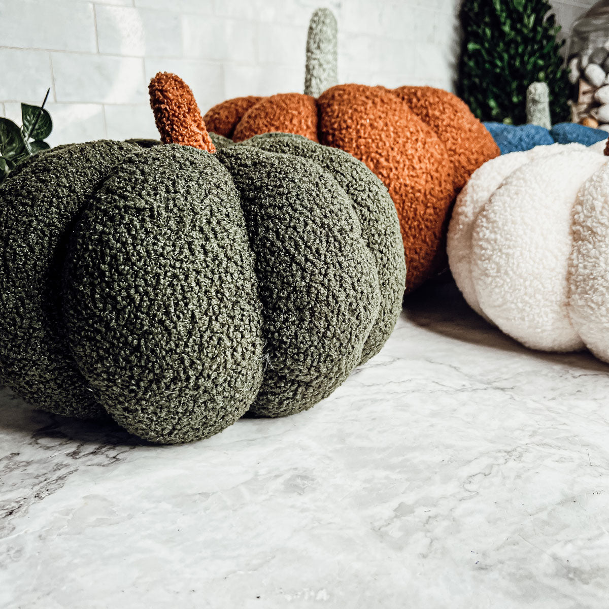 Decorative pumpkins in green, orange, and white on a marble surface.