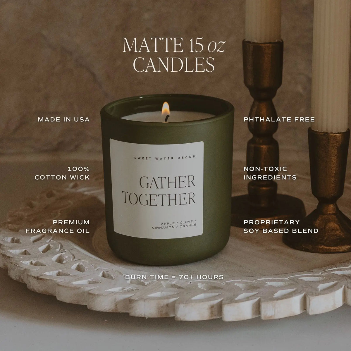A lit matte 15 oz candle in an olive green jar sits on a carved white tray, with two unlit candles in bronze holders beside it. Text overlays highlight product features such as 'GATHER TOGETHER' scent, 'MADE IN USA,' '100% COTTON WICK,' 'PHTHALATE FREE,' 'NON-TOXIC INGREDIENTS,' and 'BURN TIME = 70+ HOURS.