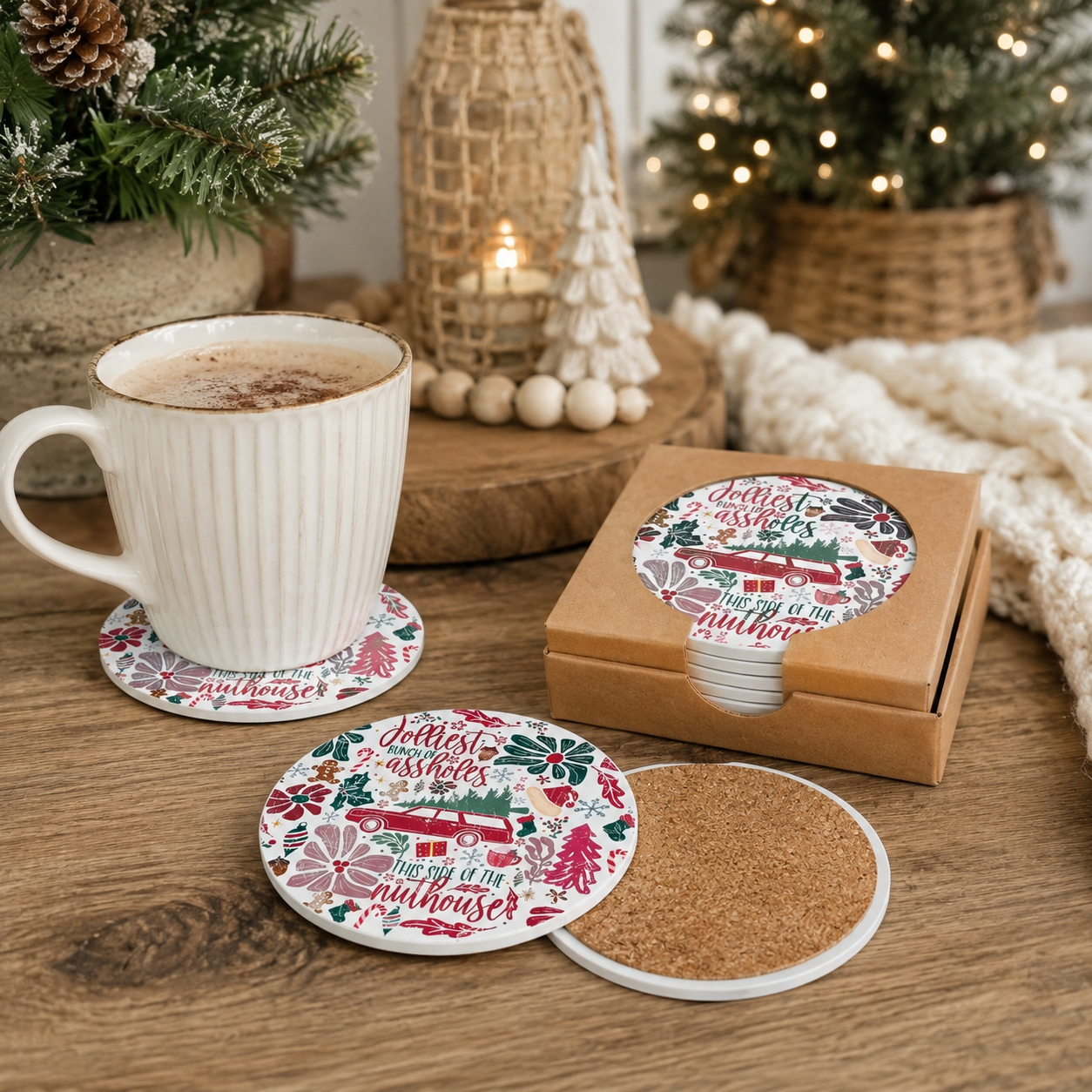 Round cork coasters with printed holiday illustrations and the phrase 'Jolly Jolly Good House' shown on a wooden table beside a white mug, with a matching coasters box in the background.