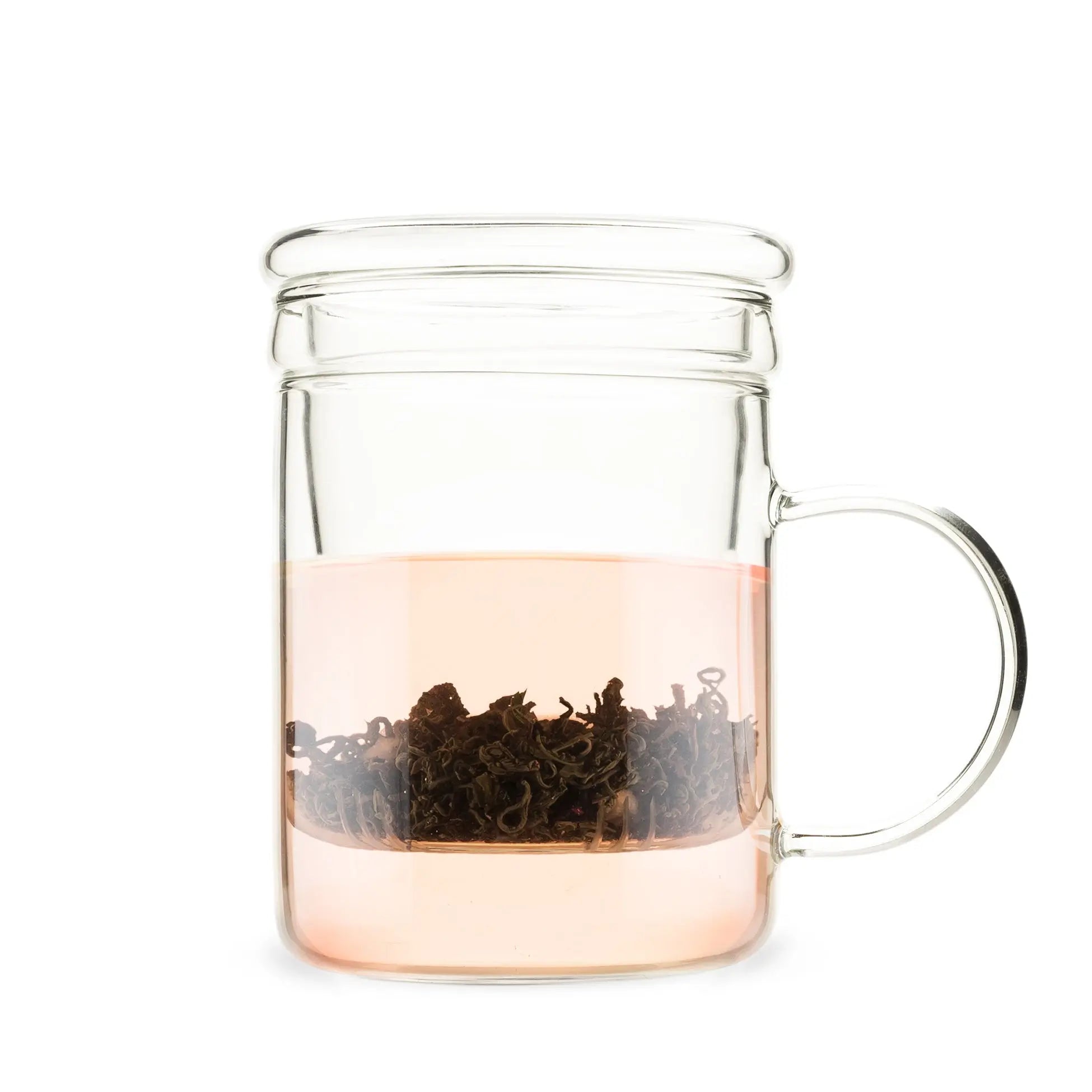 Clear glass mug with handle containing a pink liquid and black tea leaves on a white background