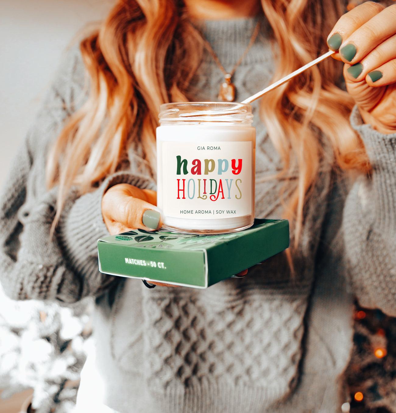 Person lighting a 'happy holidays' candle with a blurred festive background