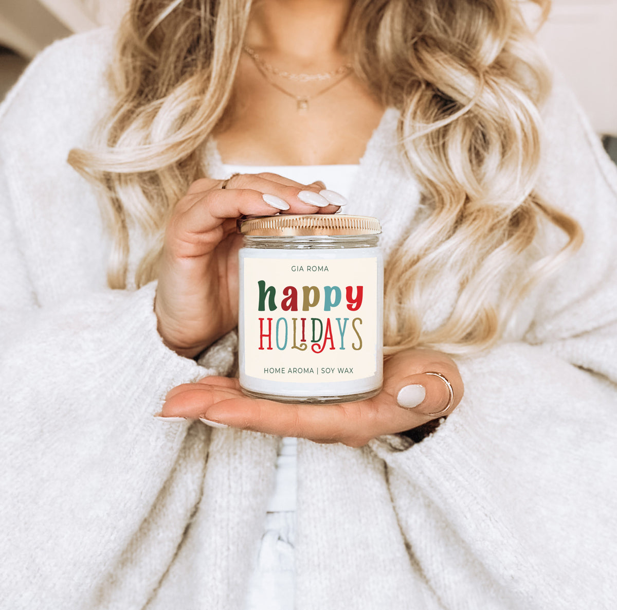 Person holding a candle labeled 'Autumn Leaves & Pumpkin Please' with a soft focus background.