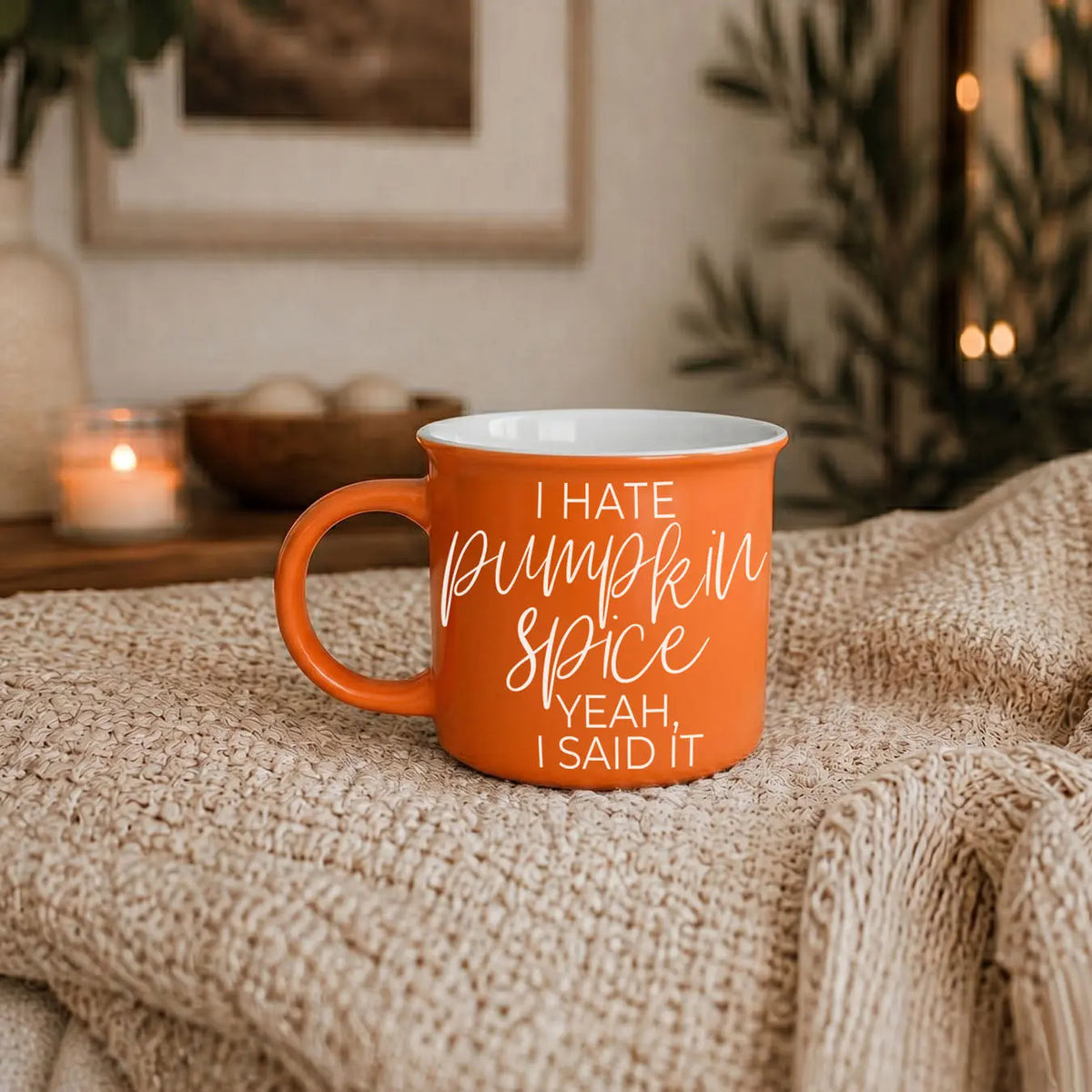 Orange mug with 'I hate pumpkin spice, yeah, I said it' text on a textured surface with a cozy background.