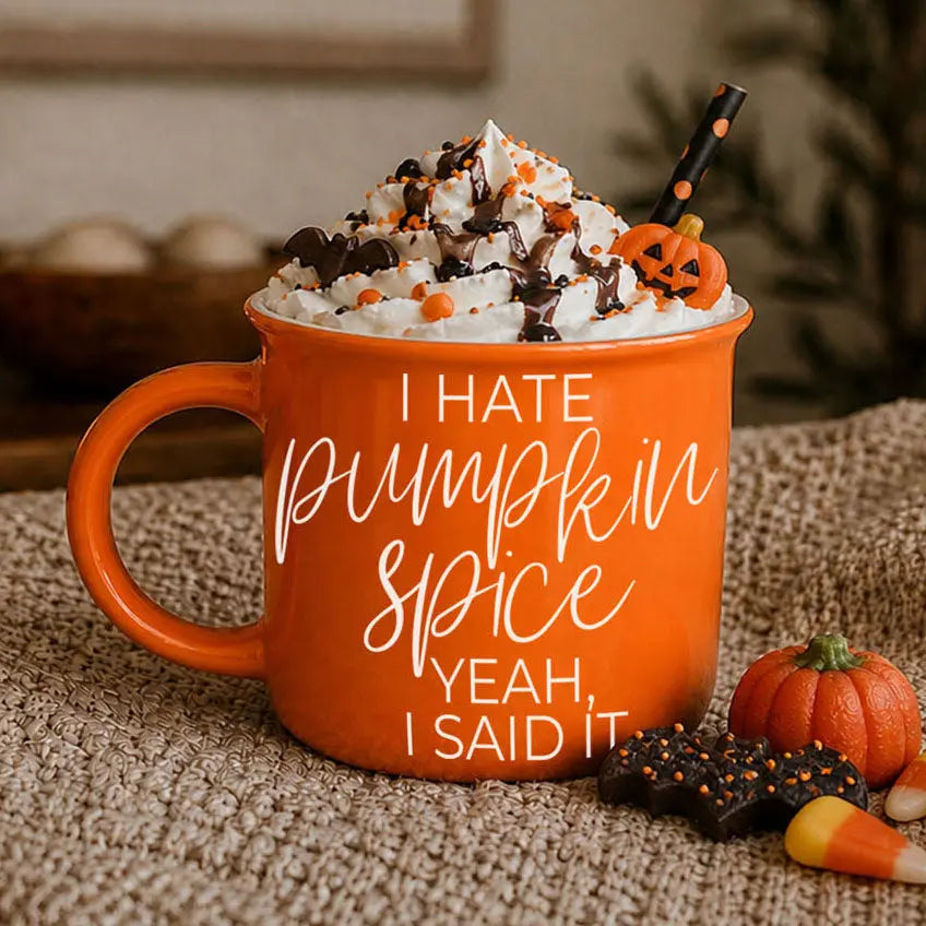 Orange mug with 'I hate pumpkin spice, yeah, I said it' text, topped with whipped cream and Halloween-themed decorations.