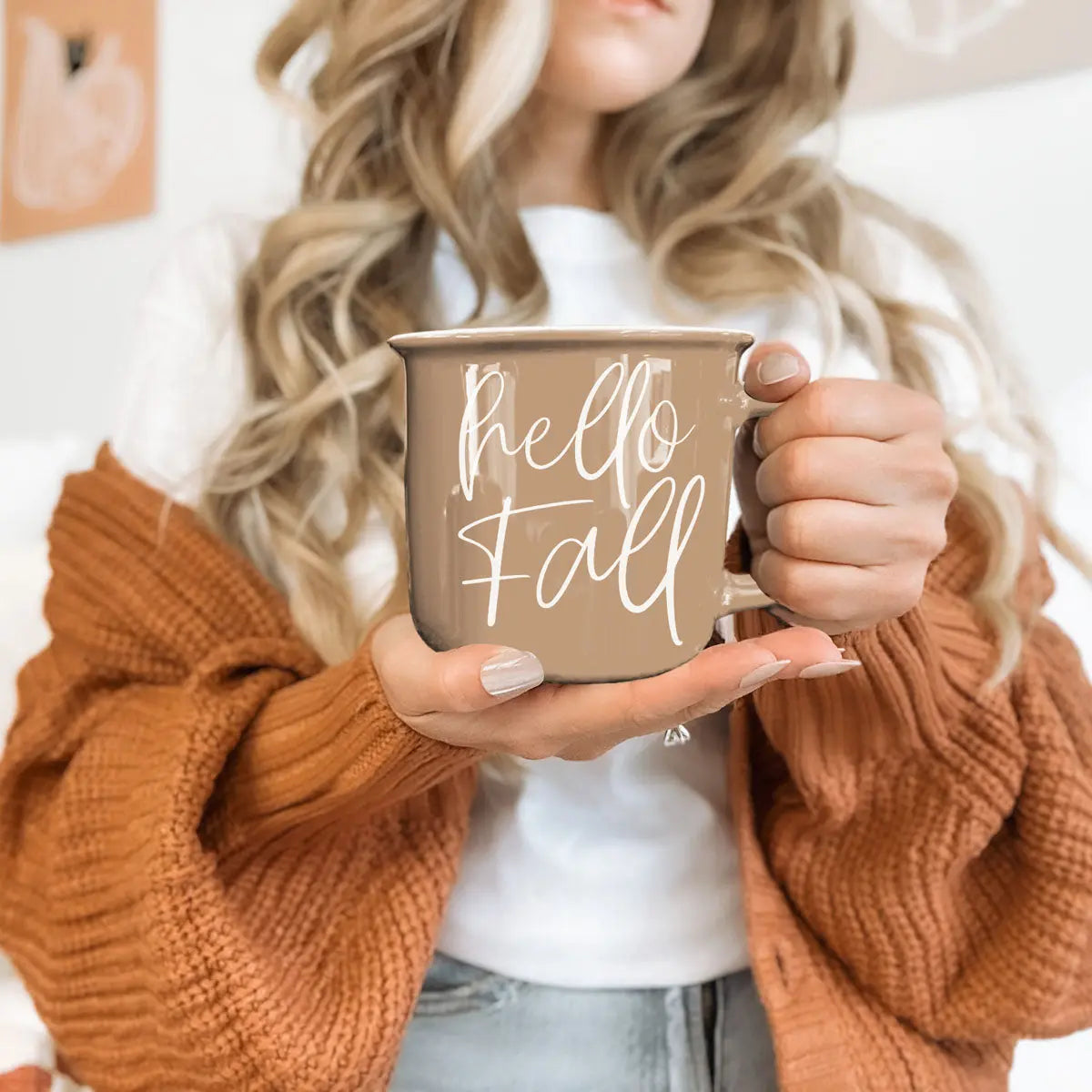Person wearing a brown sweater holding a 'Hello Fall' mug.