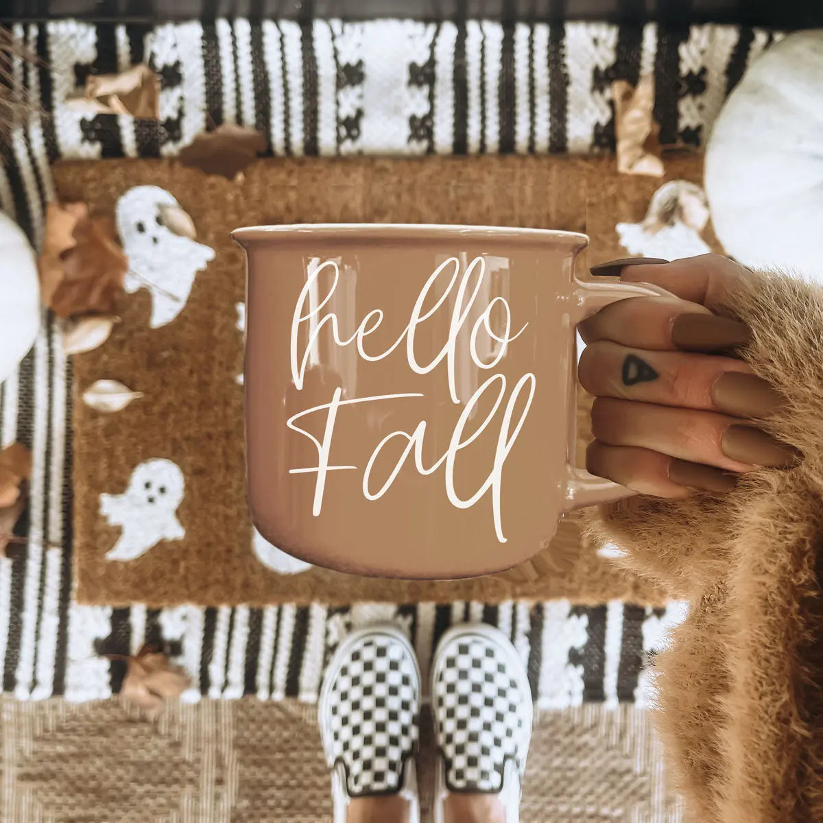 Person holding a 'hello fall' mug with a cozy background