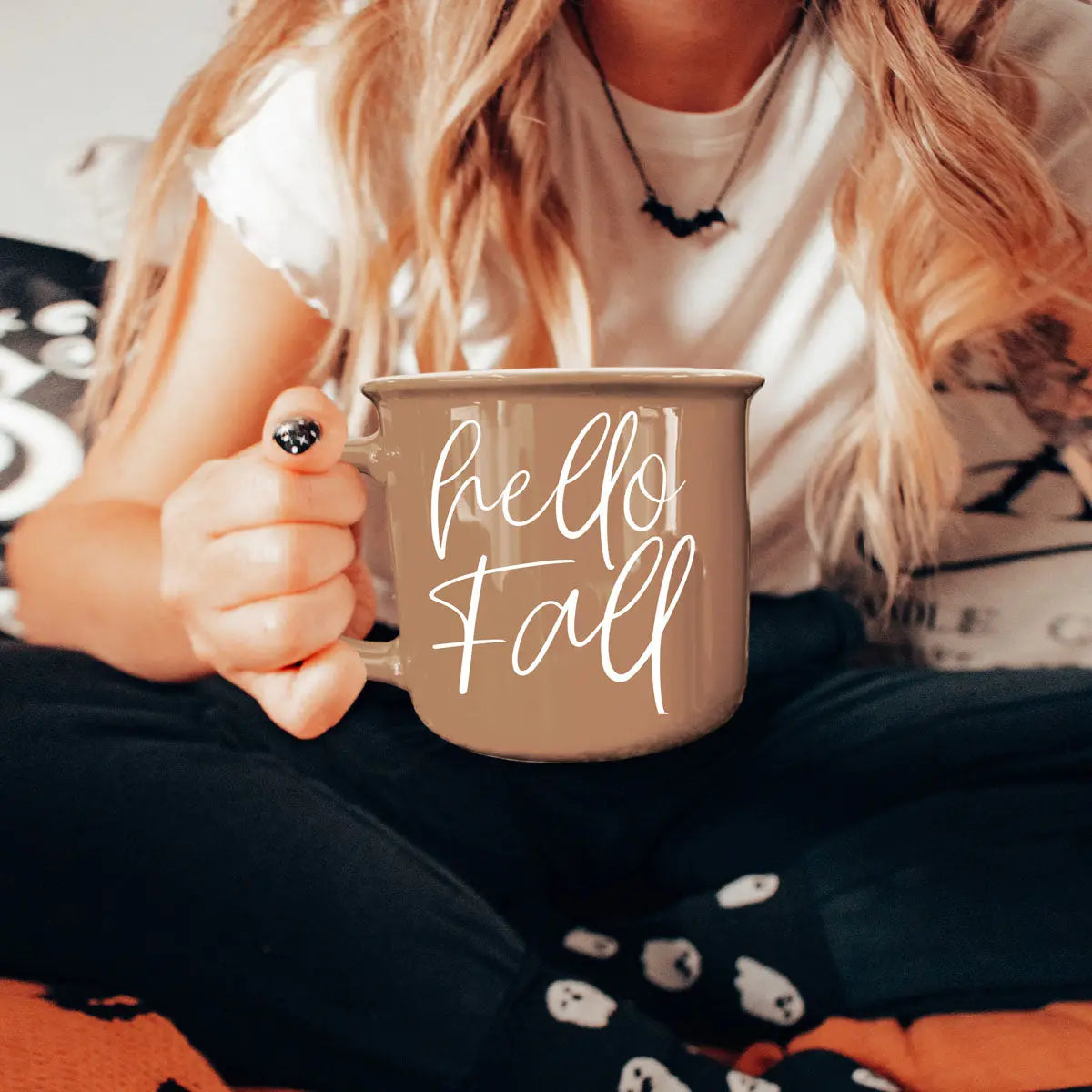 Person holding a mug with text, sitting on a couch with Halloween-themed blanket