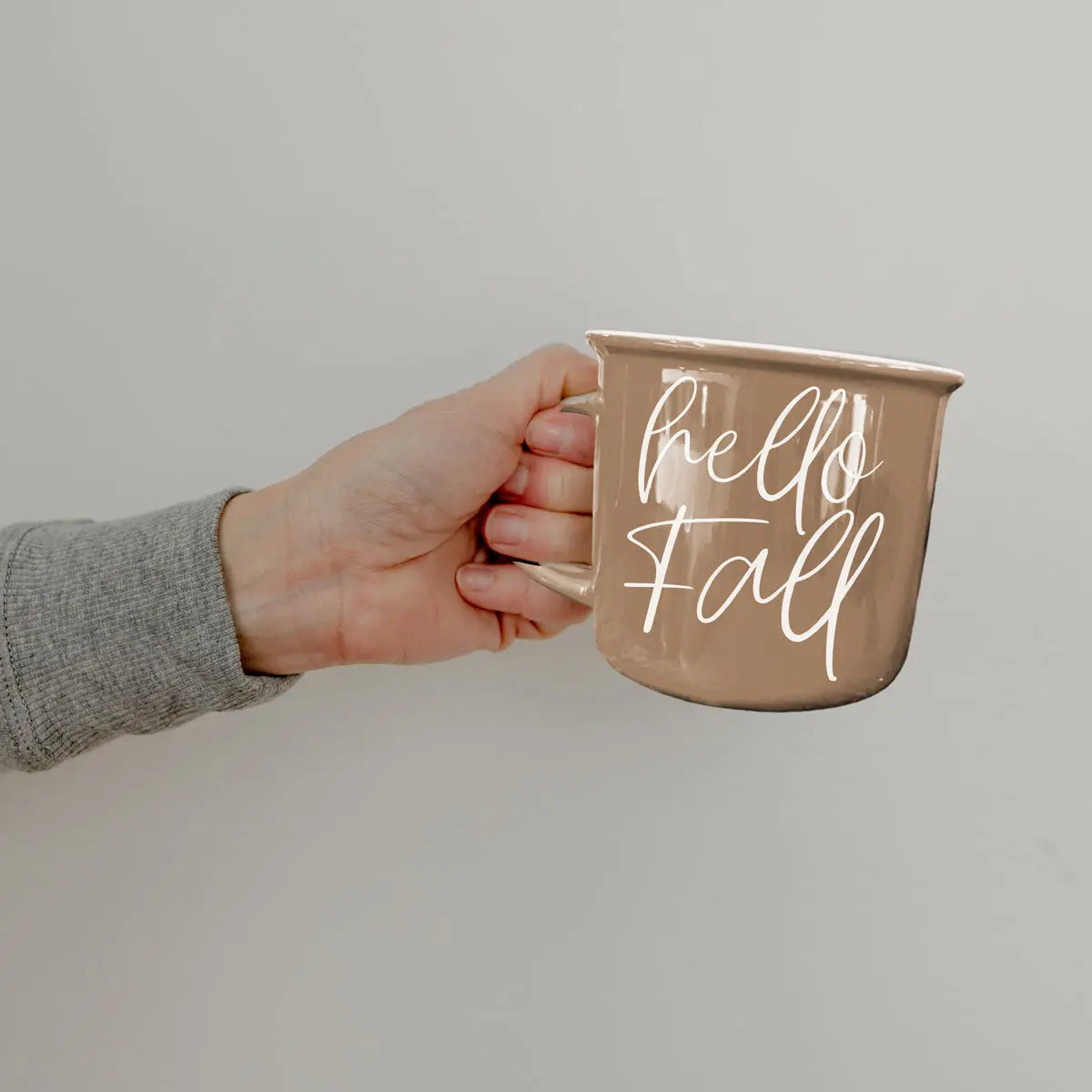 Hand holding a mug with 'hello fall' text on a plain background