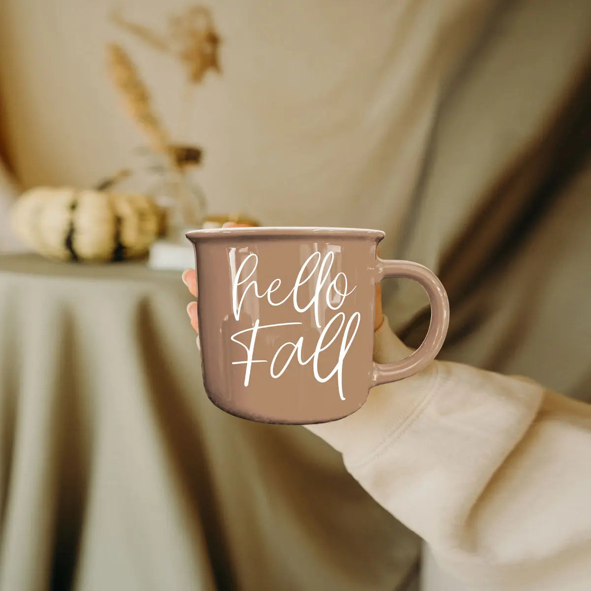 Person holding a 'hello fall' mug with a blurred autumn background