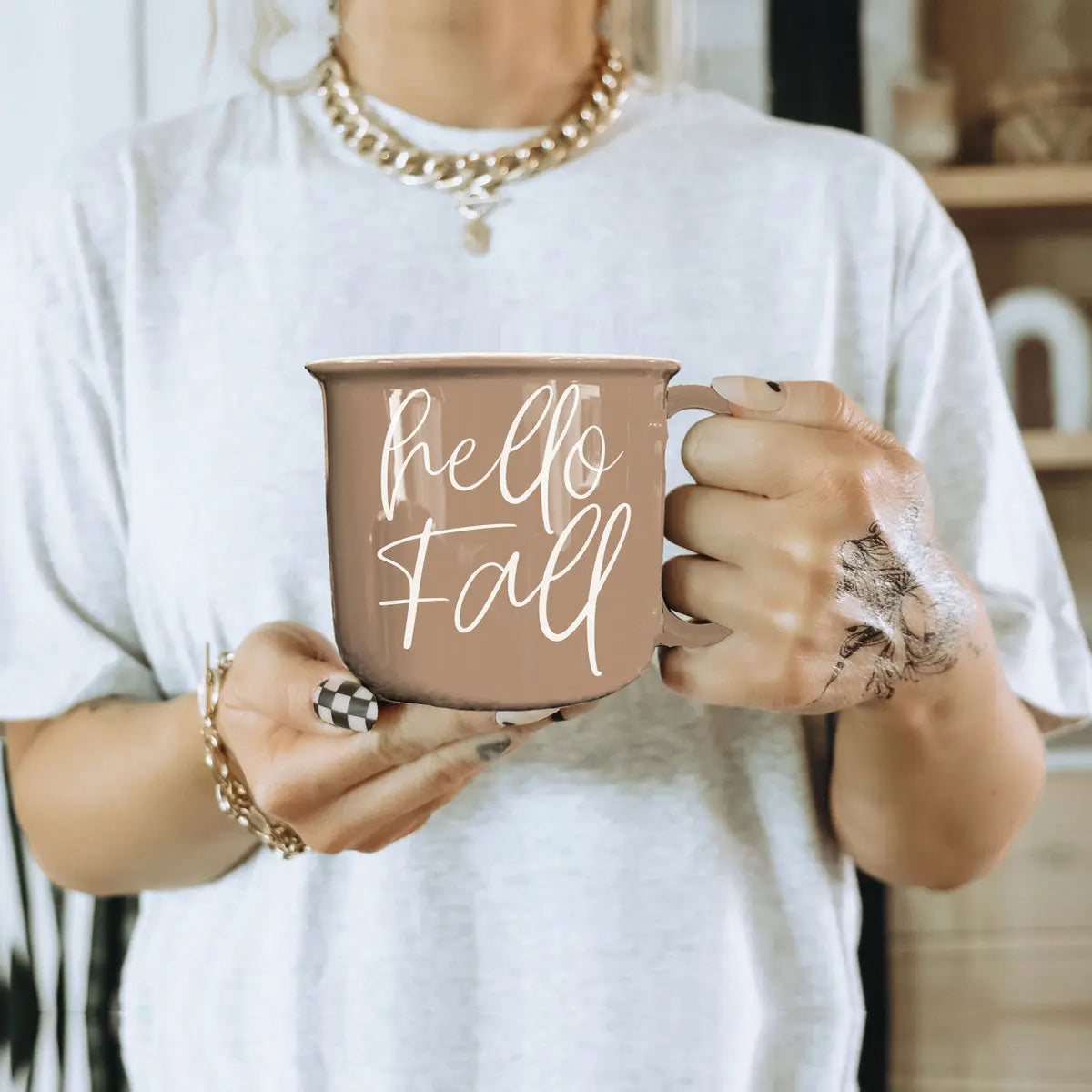 Person holding a 'hello fall' mug with a neutral background