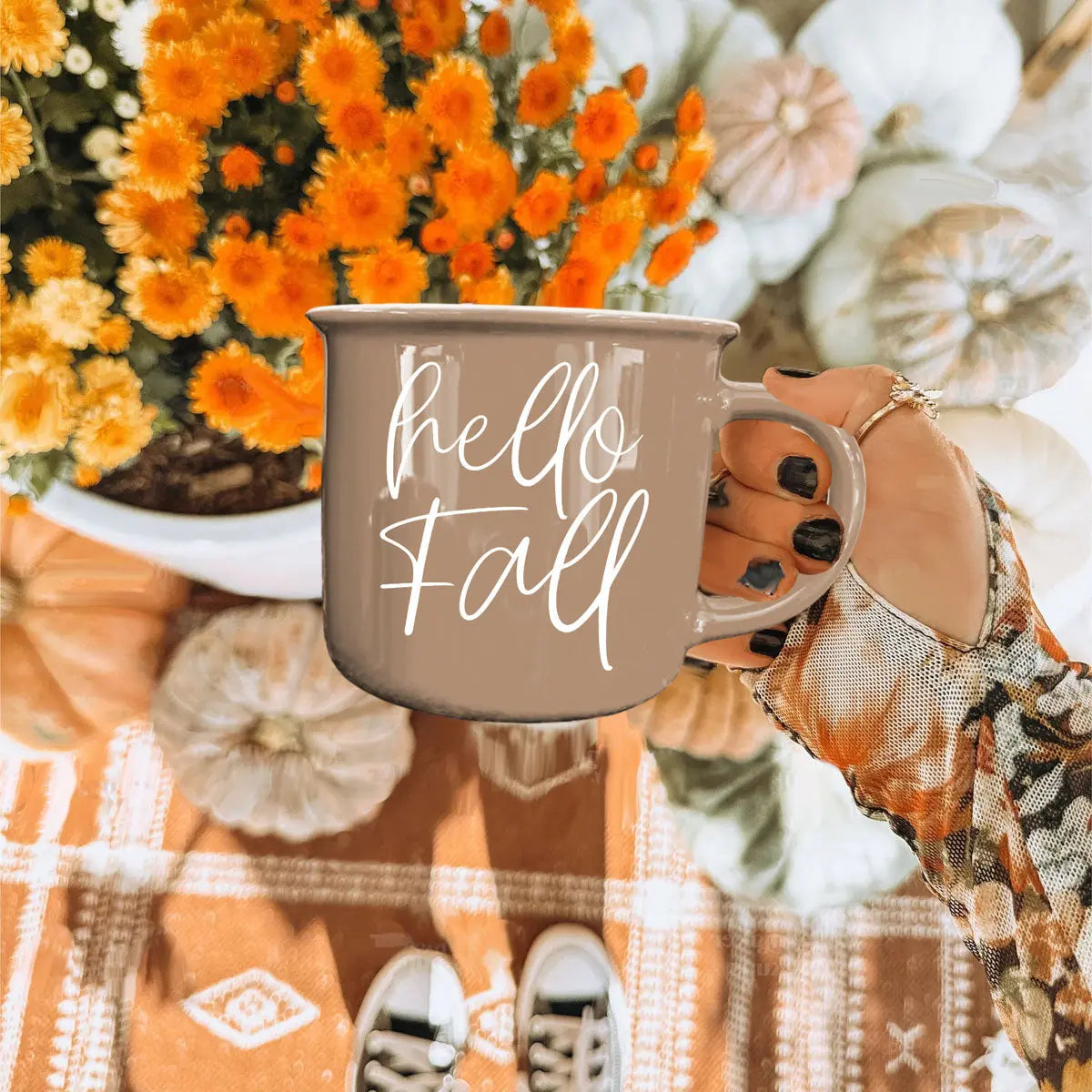Person holding a 'hello fall' mug with pumpkins and flowers in the background