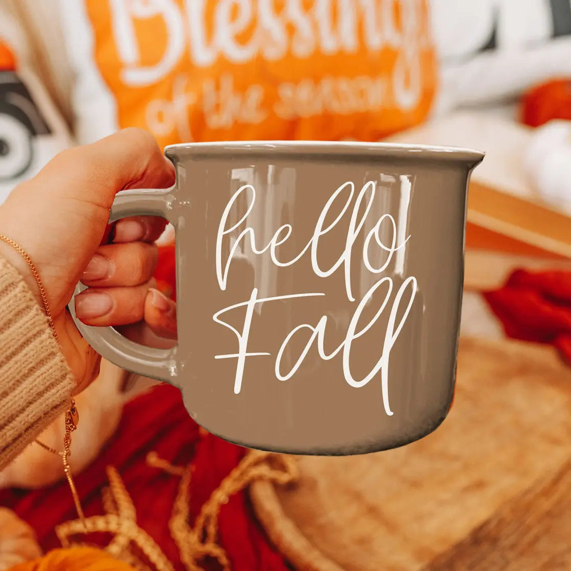 Person holding a 'hello fall' mug with autumn-themed background
