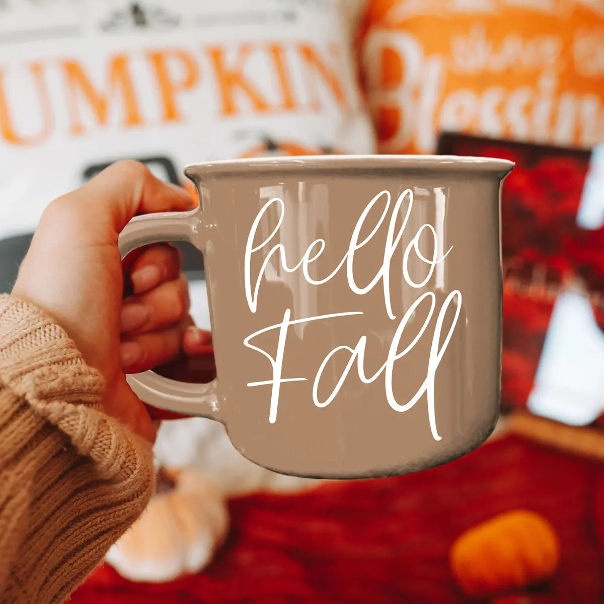 Person holding a 'hello fall' mug with autumn-themed background
