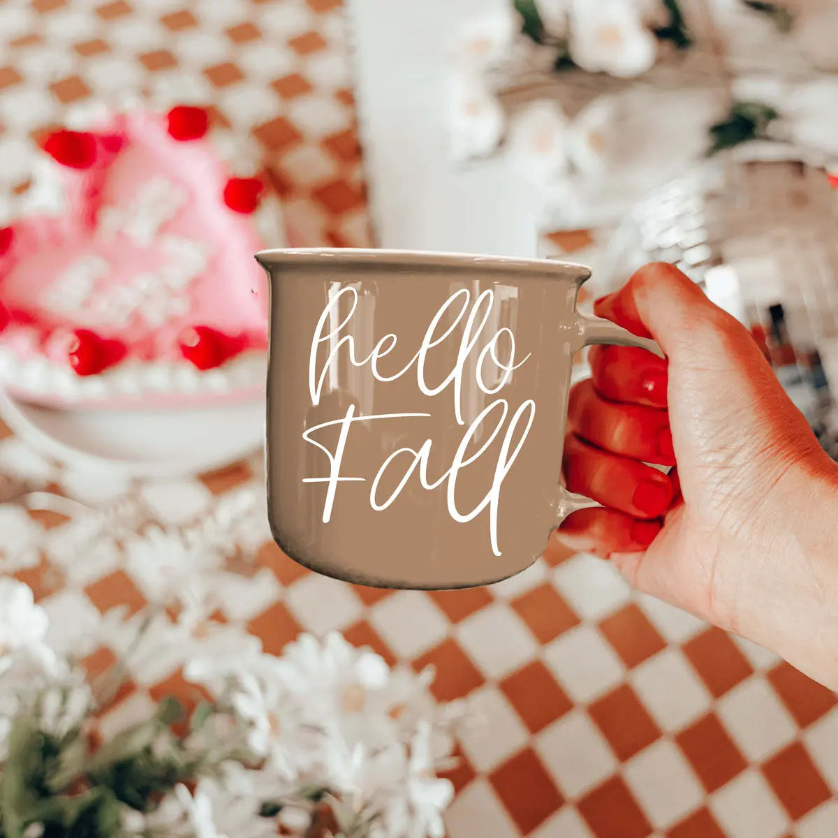 Hand holding a 'hello fall' mug with a blurred festive background