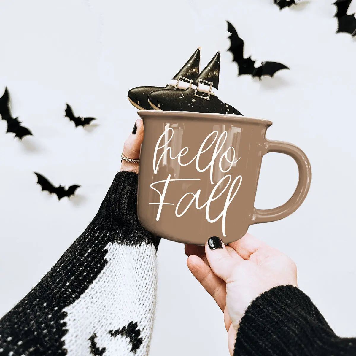 Person holding a 'hello fall' mug with decorative bats on a white background