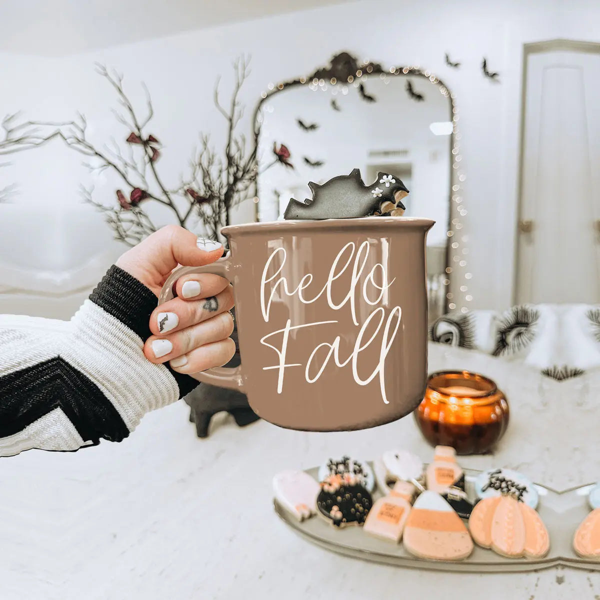 Person holding a 'hello fall' mug with Halloween-themed decor in the background