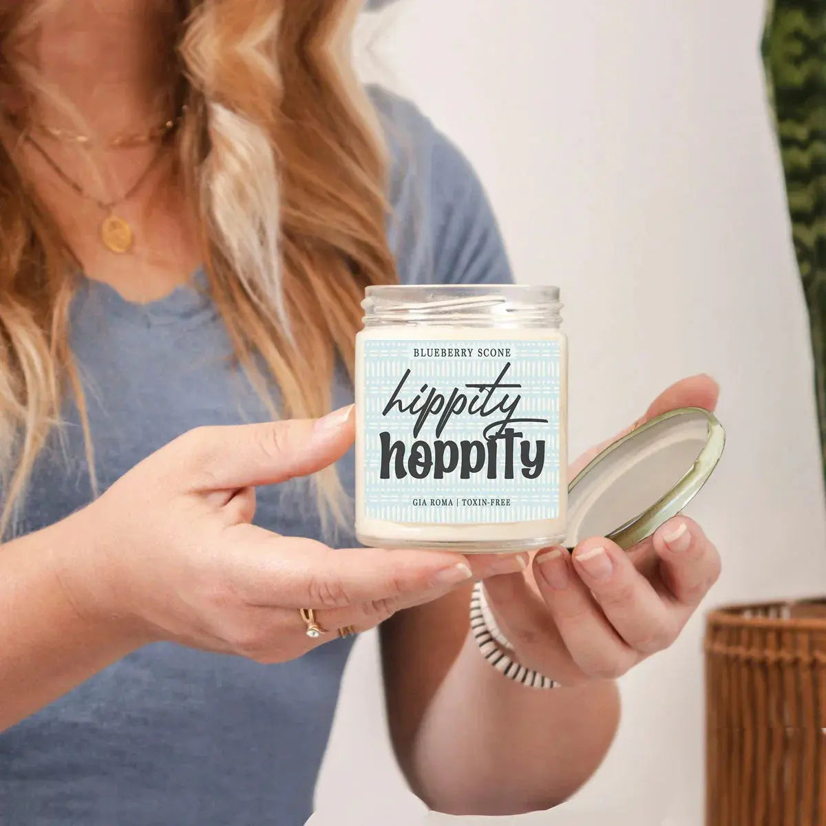 Person holding a 'hippity hippity' candle jar with a blue label.