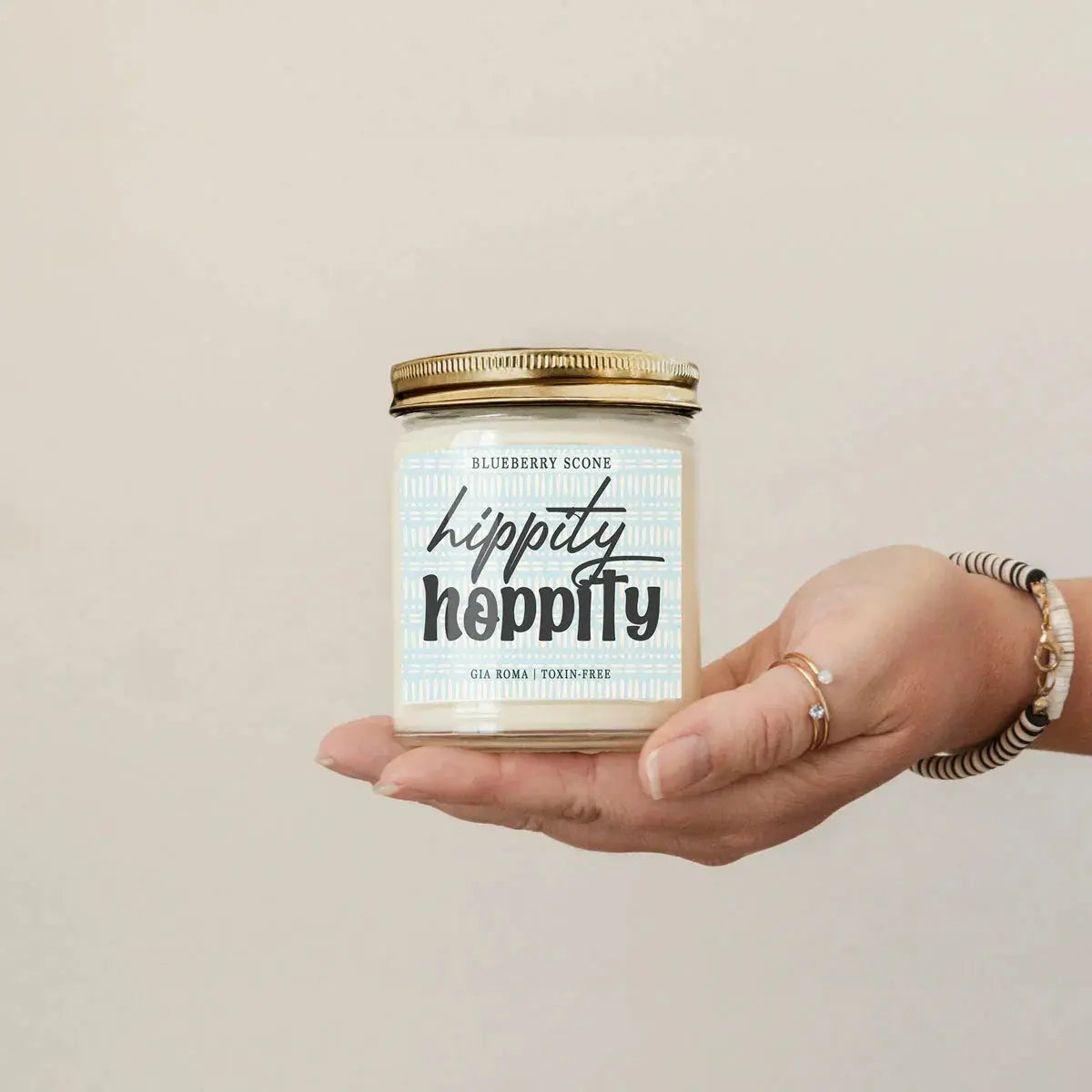 Hand holding a candle labeled 'hippity hippity' with a beige background