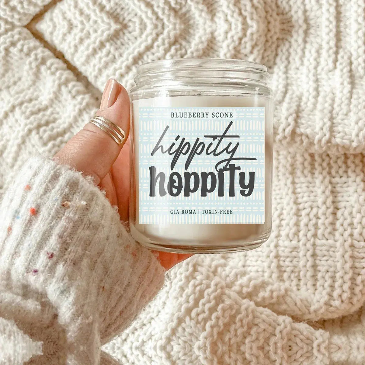 Hand holding a candle labeled 'hippity hoppity' against a textured beige background