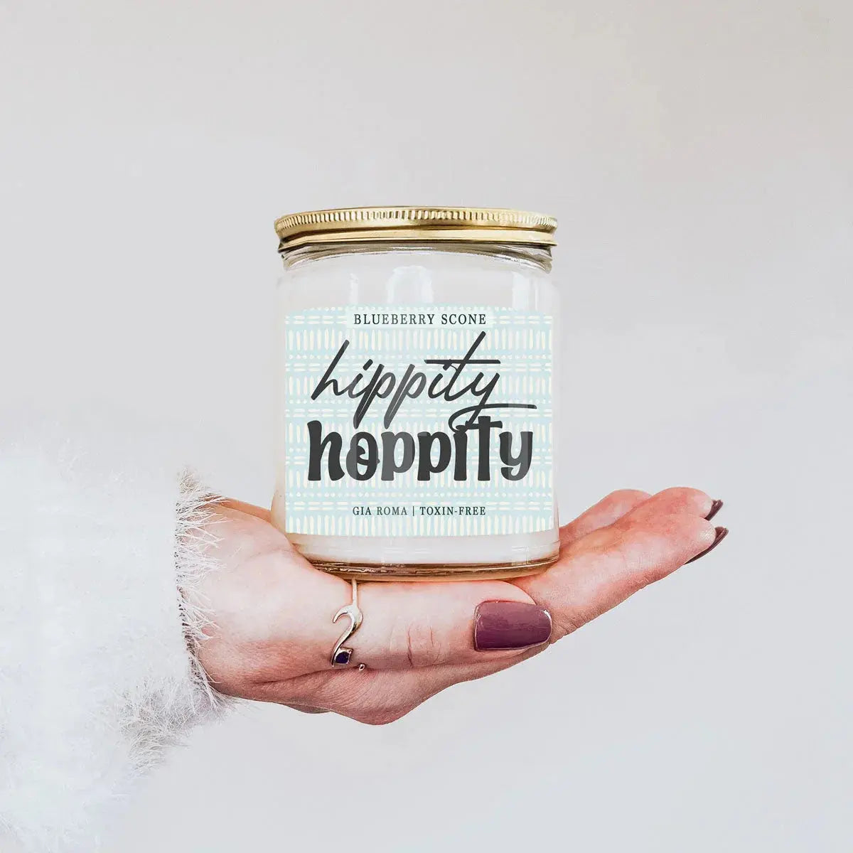 Hand holding a 'happity happity' candle jar with a white label on a light background