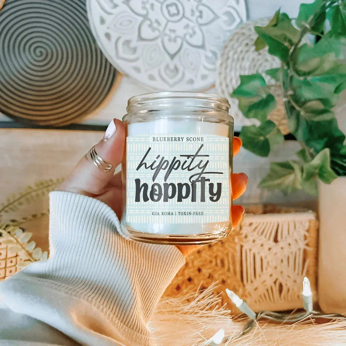 Hand holding a 'hoppity hoppity' candle jar with decorative background