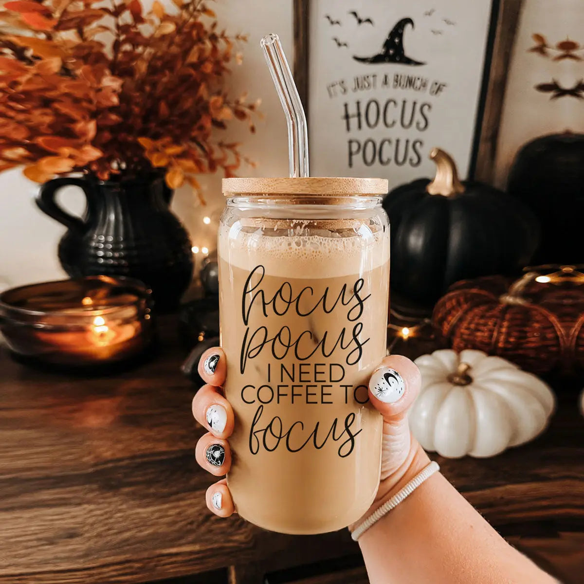 Mason jar with 'hocus pocus I need coffee to focus' text held in a hand, surrounded by Halloween decor.
