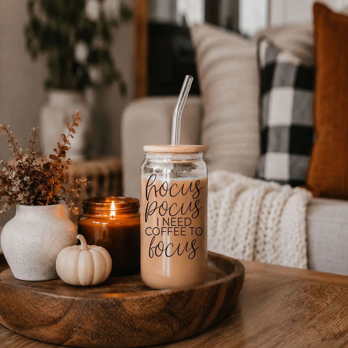 Jar with 'focus pocus I need coffee to focus' text on a wooden tray with a candle and pumpkin in a cozy living room.