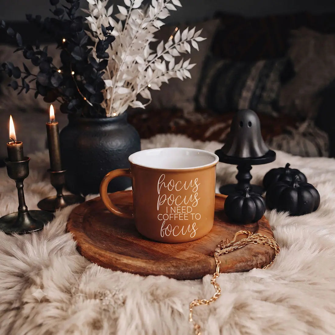 A terracotta-colored ceramic mug with a white interior and the words 'hello pumpkin' in white script, styled on a wooden tray over a white faux-fur surface with candles, pumpkins, and dried flowers in the background.