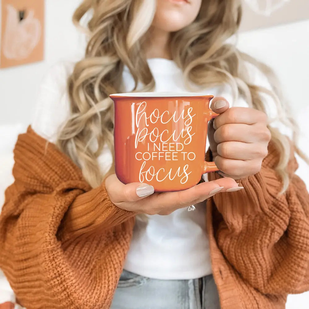Person holding an orange mug with text, wearing a brown sweater.