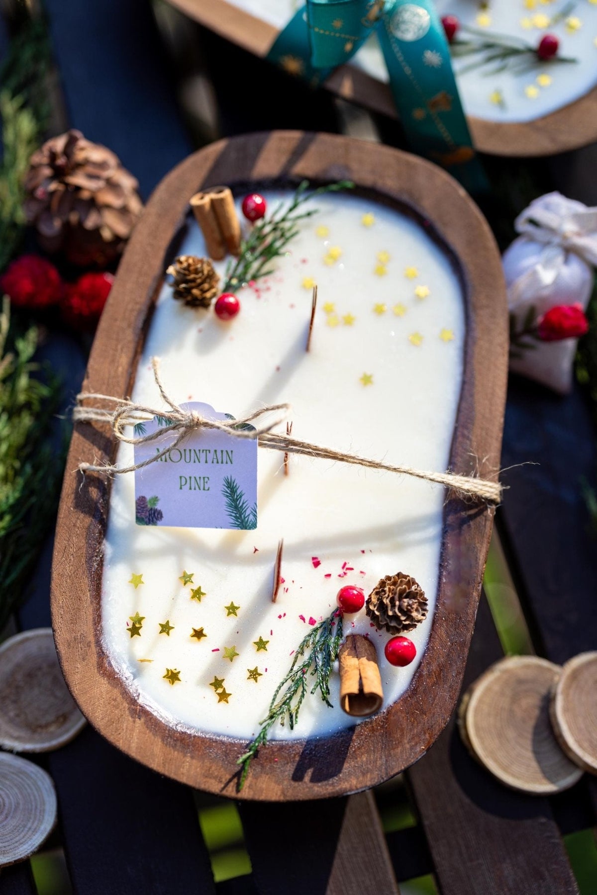 Decorative candle in a wooden holder with pine cones and red berries on a blurred natural background