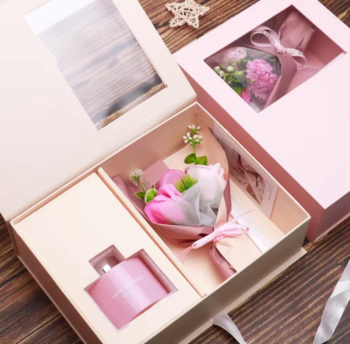 A pink gift set in a beige box, featuring a small pink bottle and a wrapped pink flower bouquet with green leaves, shown alongside a closed matching pink gift box with a clear window.