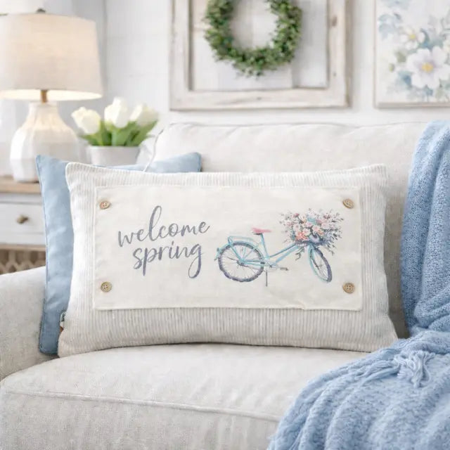 Decorative pillow with 'welcome spring' text and bicycle design on a couch.