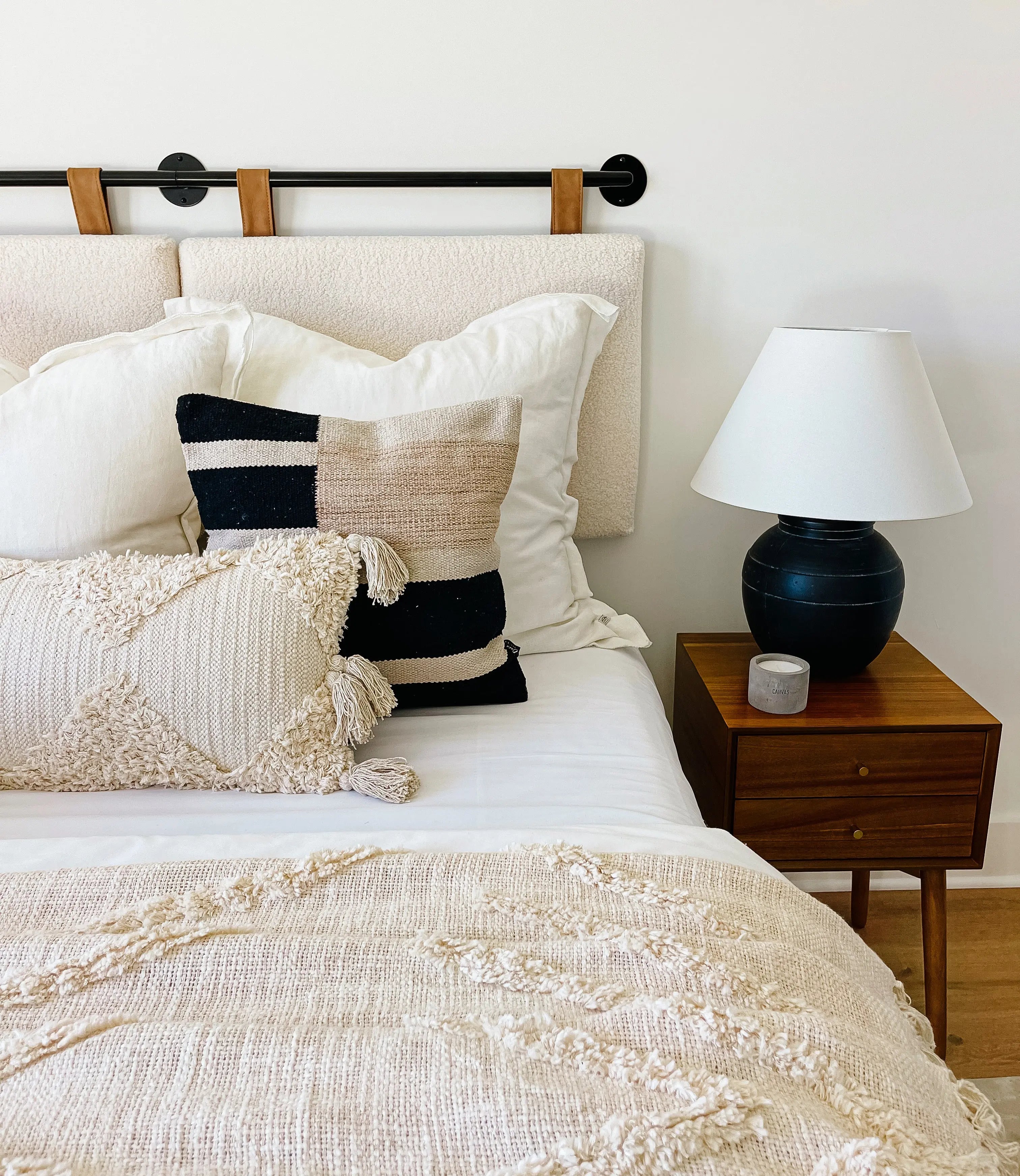 Cozy farmhouse bedroom with textured throw pillows, tassel blanket, and wooden nightstand lamp