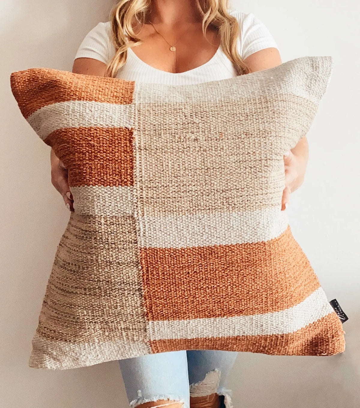Person holding a patchwork pillow with brown, beige, and white colors.