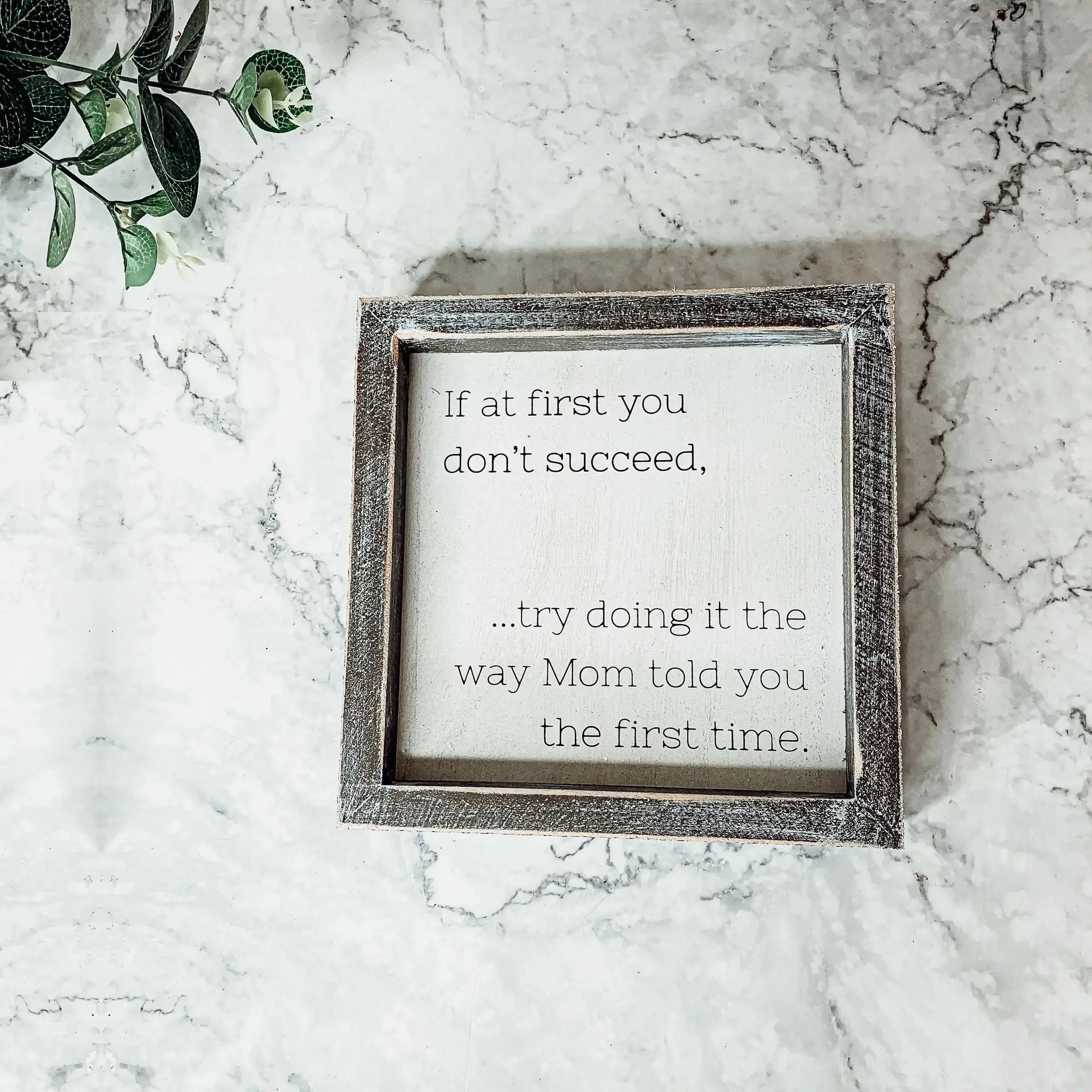 Decorative sign with motivational quote on a marble surface with greenery.