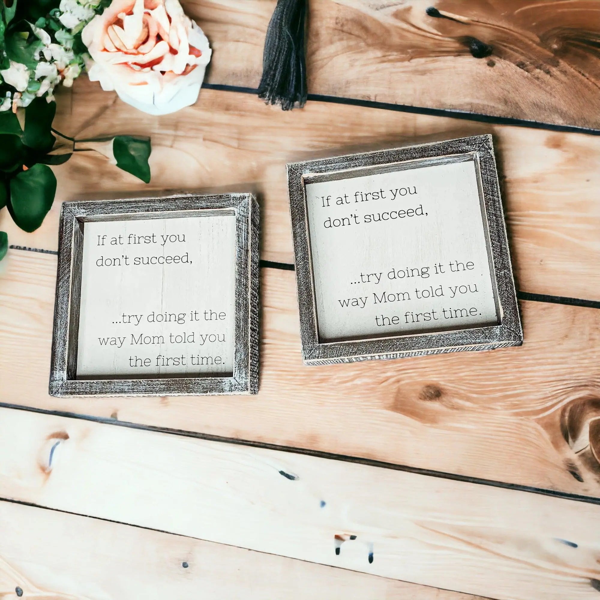Two framed quotes on a wooden surface with flowers.