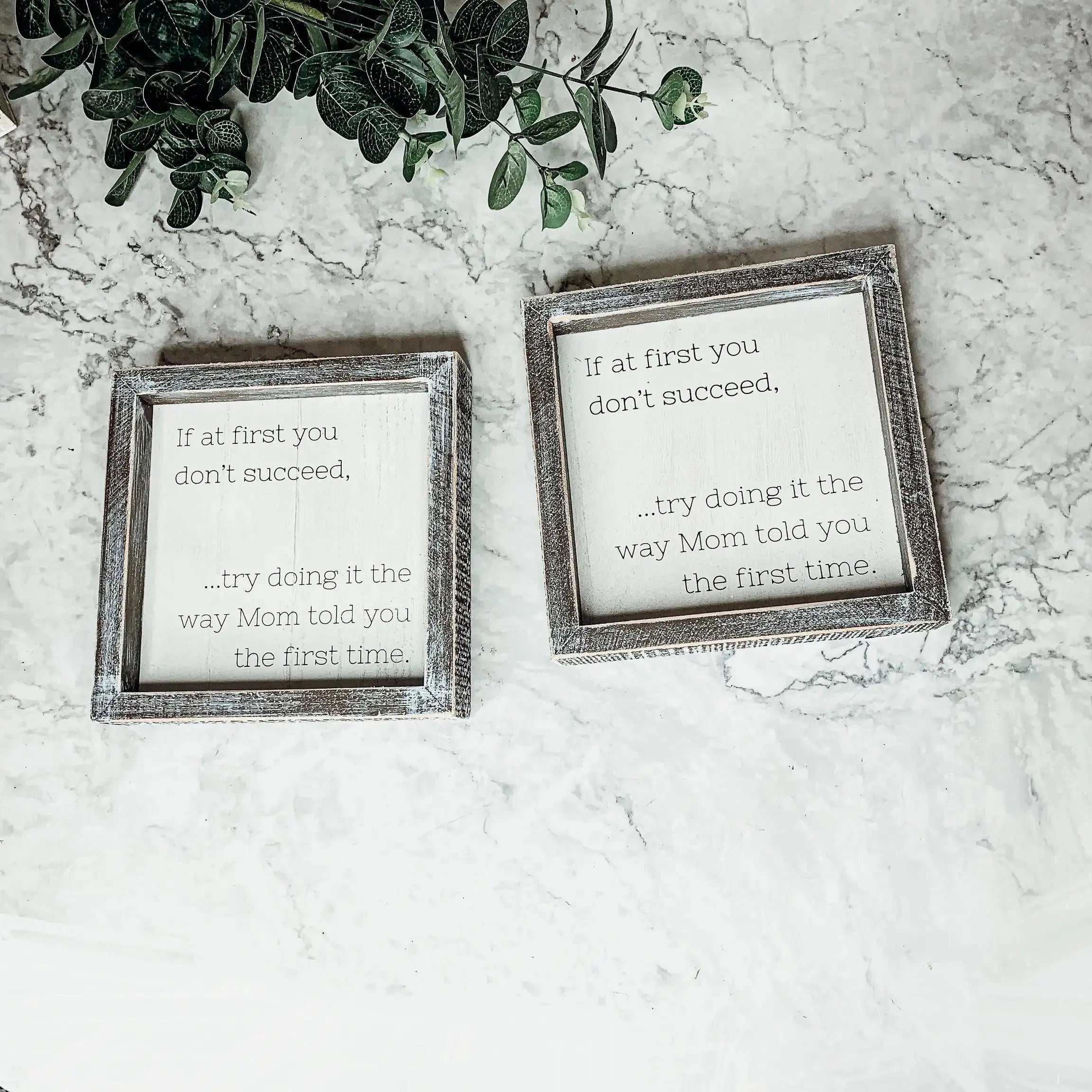 Two framed quotes on a marble surface with a plant in the corner.