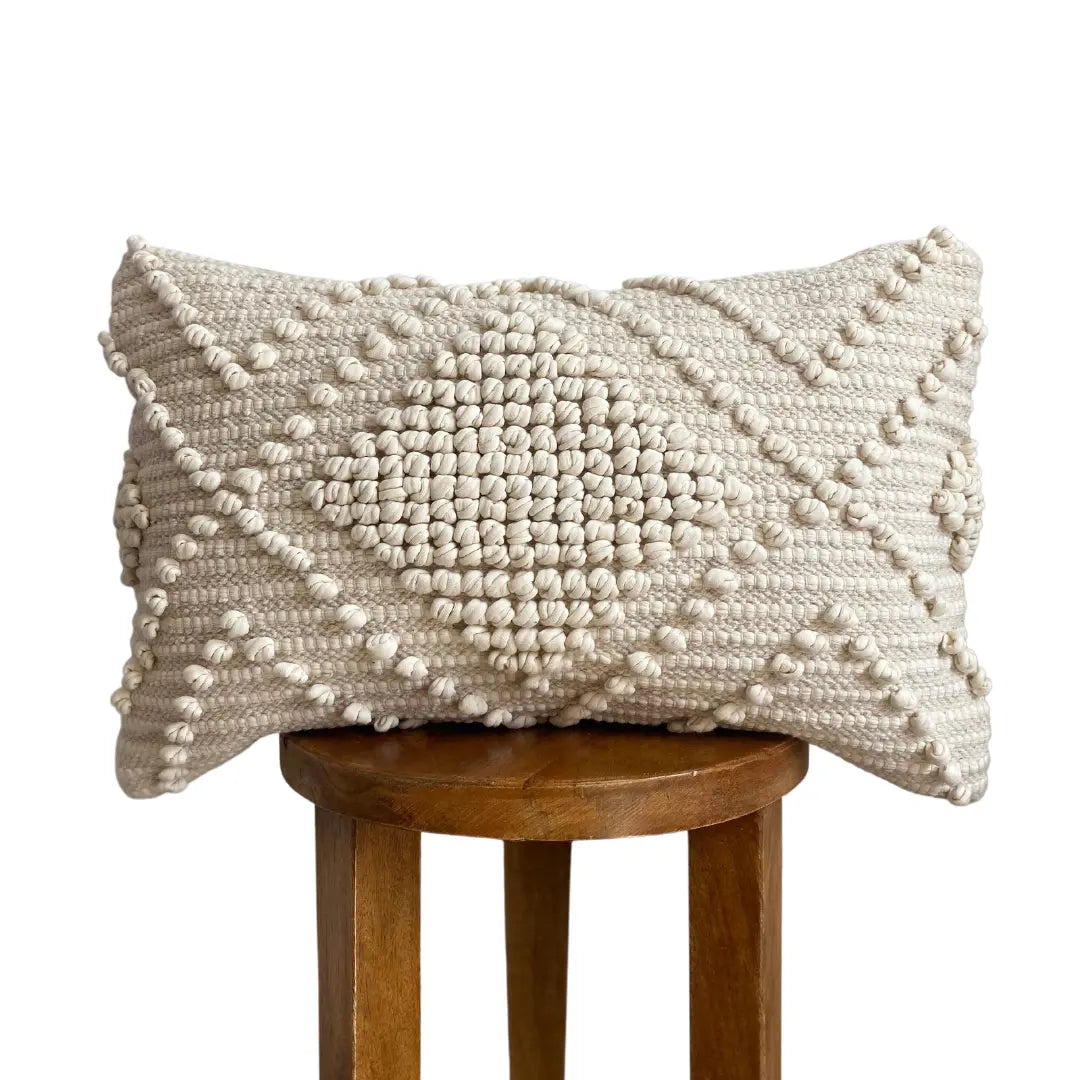 Cream textured throw pillow with woven pom-pom pattern, cozy farmhouse decor on wooden stool